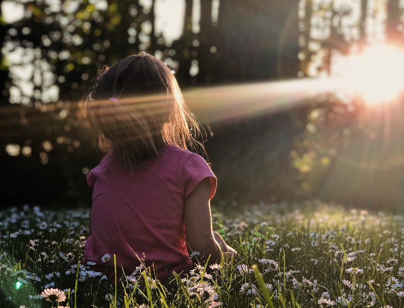 Petite fille assise dans un champ et qui contemple la nature