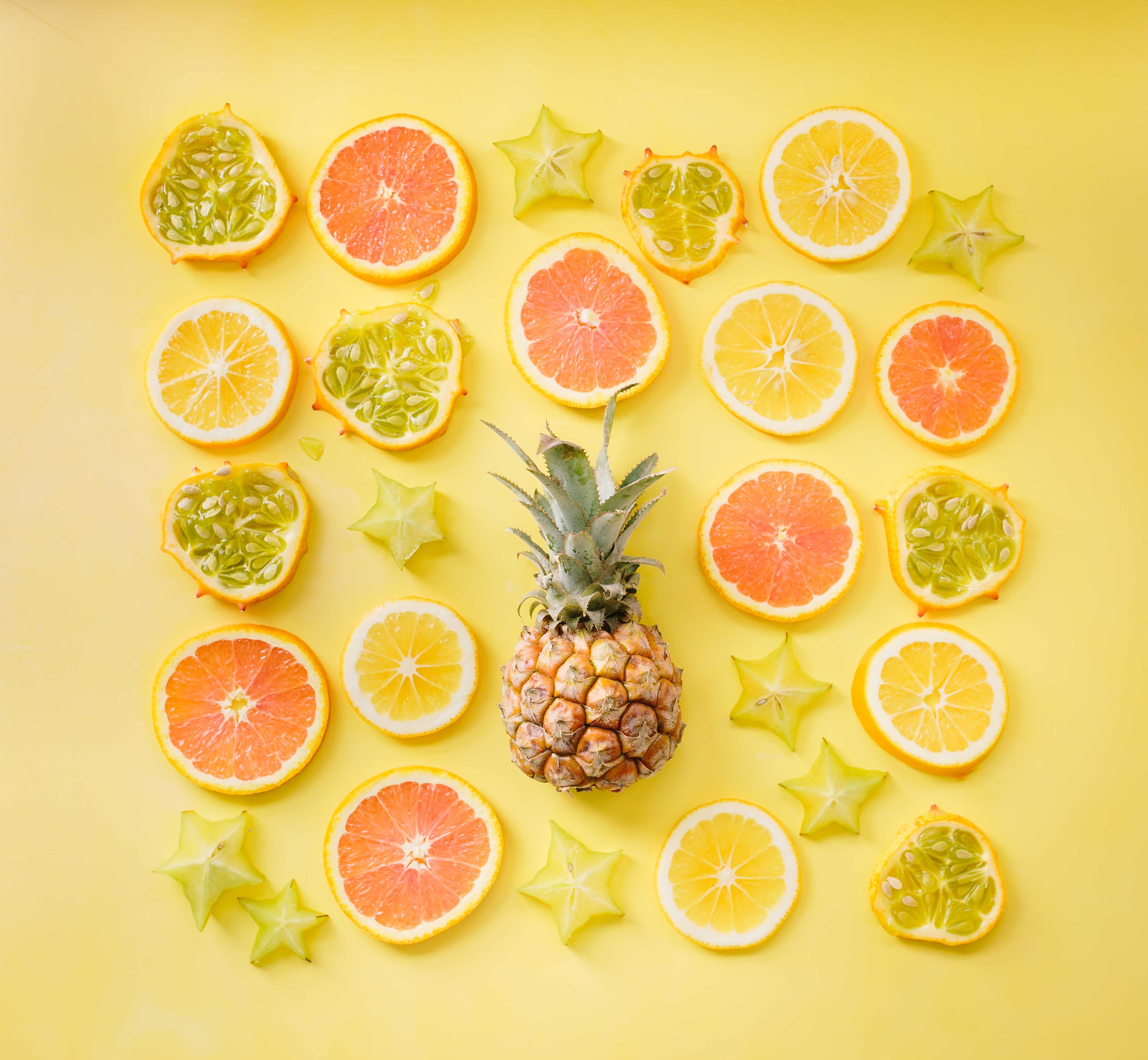 Rondelles de fruits autour d'un ananas sur fond jaune