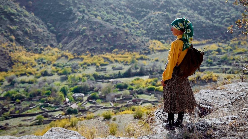 Hatidze Muratova en train de regarder un paysage montagneux et désertique. Elle porte un sac à dos contenant son équipement d'apicultrice